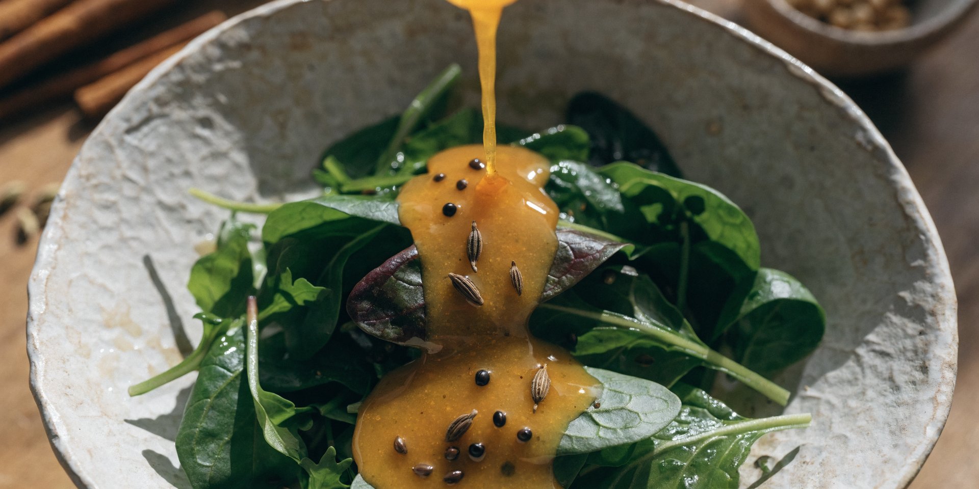 A close-up, overhead shot of a golden Indian-inspired salad dressing beautifully drizzled over a bowl of fresh mixed green salad.