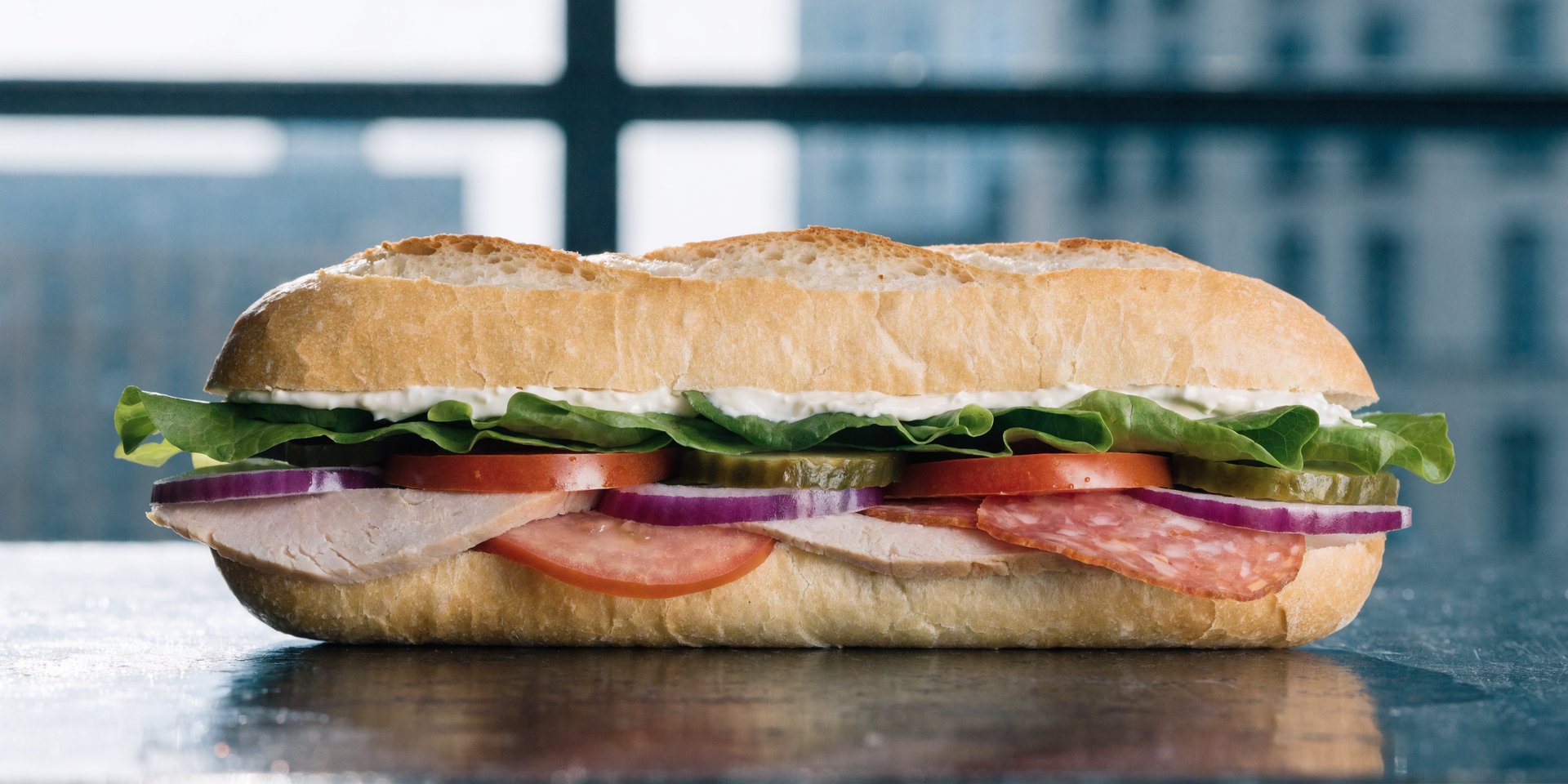 A cross-section of a deli sandwich, showing a layer of spread protecting the bread from moist fillings like tomato and lettuce.