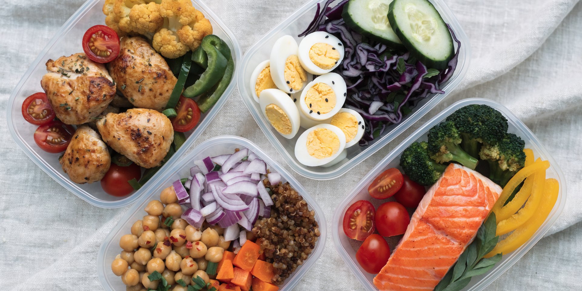 An overhead view of several meal prep containers filled with various high-protein lunches, including chicken, salmon, eggs, and vegetables.